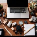 A table with various DIY home decor subscription boxes spread out, surrounded by crafting materials and tools. Magazines and design inspiration scattered around